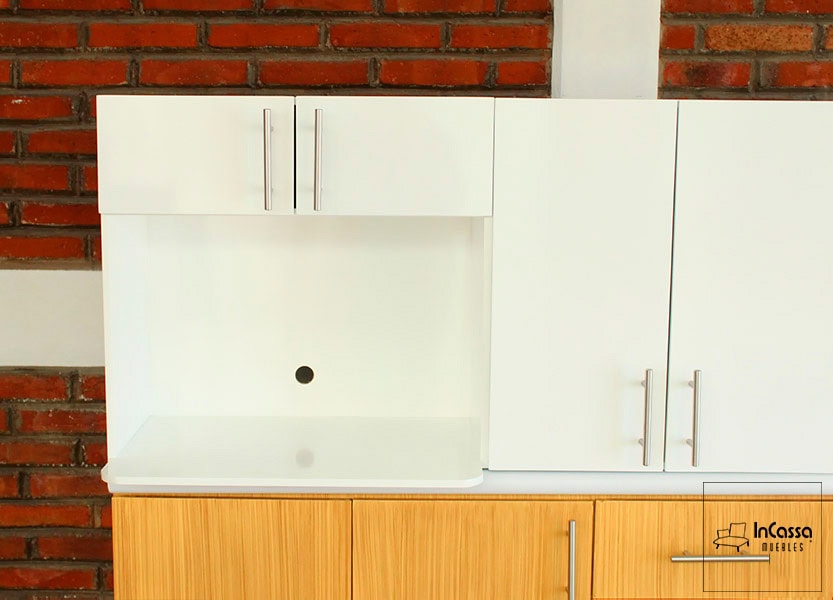 La foto se concentra principalmente en la alacena superior blanca, en la que destaca su espacio porta microondas. Cada puerta cuenta con una jaladera de barra T incorporada.