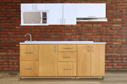 Moderna cocina integral instalada junto a una pared de ladrillos; la cocina cuenta con un módulo inferior largo diseñado para parrilla con acabado natural, además de una alacena superior con espacio para microondas y un módulo sobre campana, ambos módulos superiores son de color blanco.