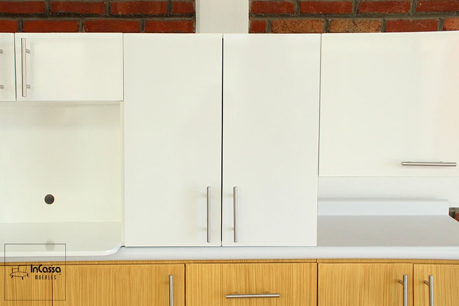 Una vista cercana de los módulos superiores de color blanco, entre los cuales vemos un mueble sobre campana y una gran alacena superior que además cuenta con porta microondas. Cada módulo cuenta con jaladeras de barra T en todas sus puertas.