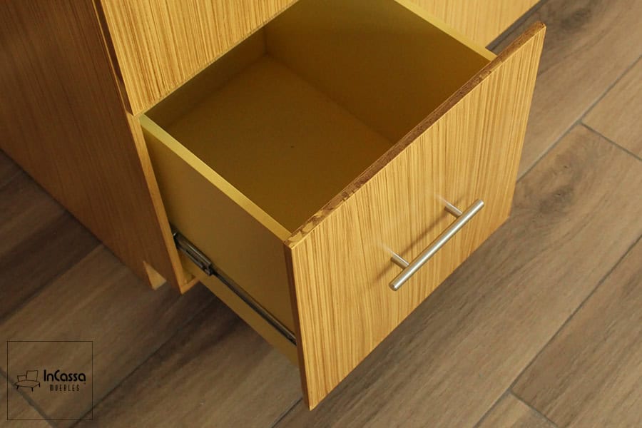 Un vistazo al interior de uno de los cajones, siendo este bastante profundo y espacioso. Además se puede ver uno de sus rieles metálicos y su jaladera de barra T, los cuales conforman el sistema de apertura y cierre del cajón, mismo que conserva el mismo tono natural en la totalidad de su estructura.