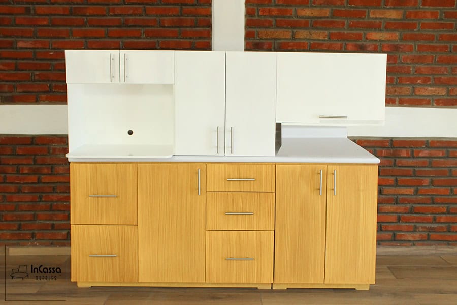 La foto muestra todos los módulos que conforman la cocina, siendo los superiores de color blanco de los cuales destaca la alacena superior con porta microondas, mientras que el módulo inferior largo tiene un acabado natural y cuenta con una cubierta de formaica blanca.