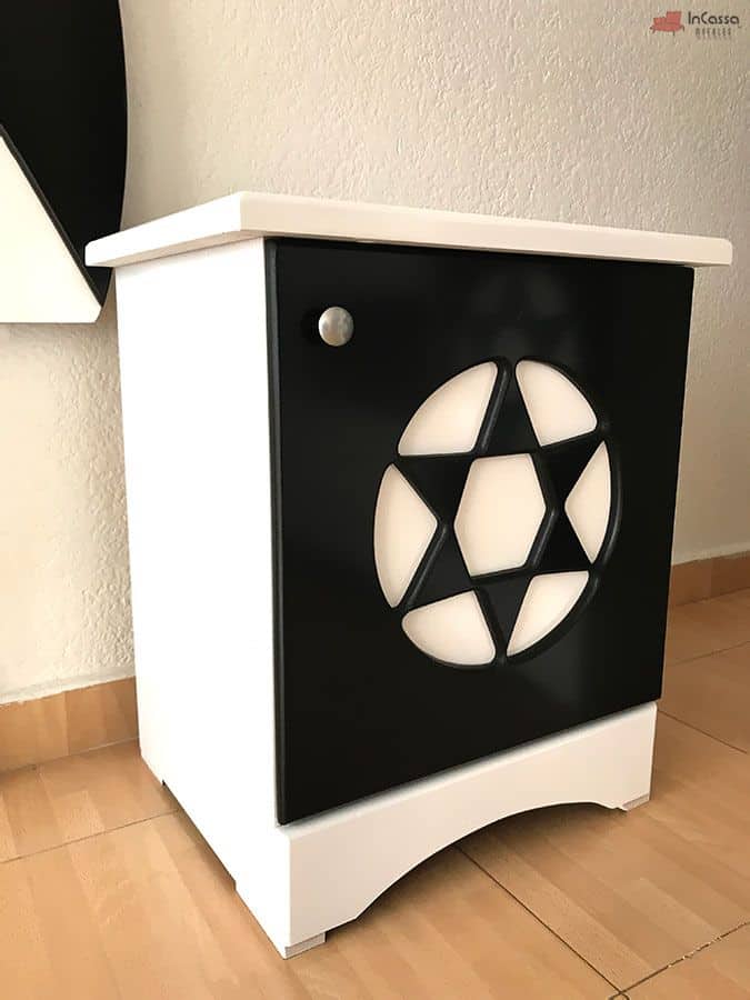 La fotografía en primer plano resalta el buró blanco con frente negro decorado con figura de balón en blanco, herraje metálico y acabado brillante. Un toque moderno y deportivo para ambientar recámaras juveniles temáticas.