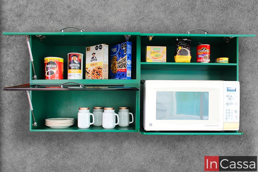 Foto frontal del módulo superior de la cocina, el cuál cuenta con tres compartimentos con puertas de apertura y cierre vertical gracias a pistones neumáticos; el módulo destaca gracias a su espacio para microondas, además de que mantiene el color verde en la totalidad de su estructura.