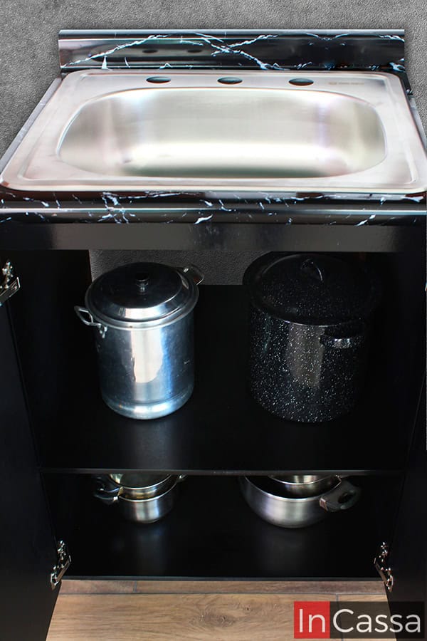 Imagen del módulo inferior con tarja incluido en la cocina; presentado con sus puertas abiertas mostrando dos amplios espacios para guardar utensilios de cocina. El mueble cuenta con una cubierta de formaica negra, al igual que el resto de su estructura.