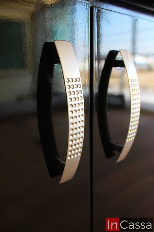 Foto cercana de las jaladeras integradas a las puertas de la cocina, estas son metálicas con un moderno diseño de arco. La cercanía de la toma también permite apreciar el acabado brillante de la pintura negra del módulo.
