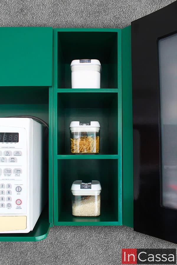 La foto muestra 3 de los estantes abiertos que pueden encontrarse en el módulo esquinero superior incluido en la cocina, los cuales son de color verde, al igual que el resto del módulo, y están divididos por entrepaños, ofreciendo prácticos espacios adicionales para guardar especias y otros consumibles de cocina.