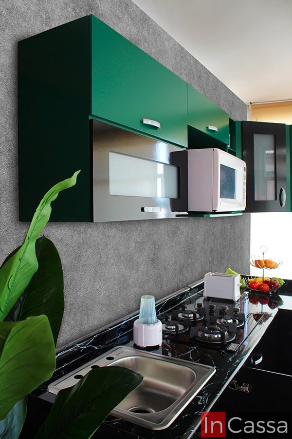 Foto lateral de la cocina, la cual destaca sus módulos superiores de color verde, así como la cubierta de formaica en estilo mármol negro y la tarja sencilla de acero inoxidable que pueden encontrarse en los módulos inferiores.