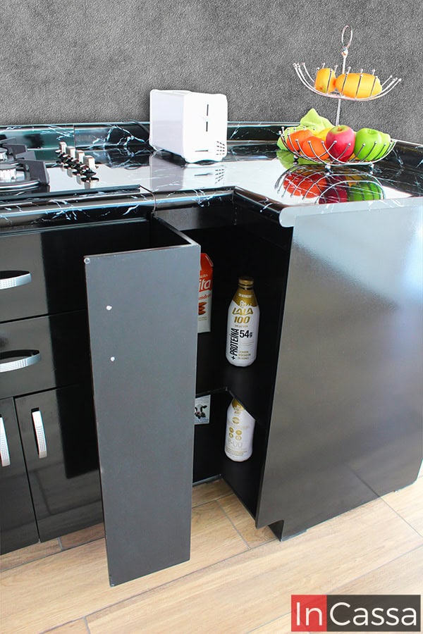 La foto destaca el módulo esquinero inferior incluido en la cocina, el cuál es de color negro en su totalidad y cuenta con una cubierta de formaica en estilo mármol negro. Además el modulo cuenta con dos compartimentos para almacenar alimentos enlatados o bebidas embotelladas, estos ocultos por una puerta en L.