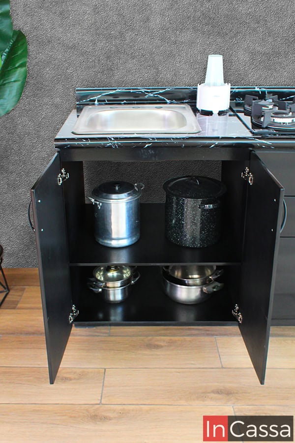 Foto frontal de la sesión de tarja del módulo inferior largo incluido en la cocina, la cuál se presenta con sus puertas abiertas, dejando a la vista 2 amplios compartimentos para almacenar utensilios de cocina. El módulo es de color negro en acabado brillante, color que se conserva igualmente en los interiores del mueble, así como en su cubierta de formaica.