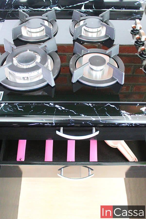 Fotografía desde una toma superior del módulo inferior de la cocina, concentrándose en la sección de parrilla la cuál cuenta con dos cajones, de los cuales el superior es estético mientras que el inferior es funcional ofreciendo un espacio para guardar utensilios. Ambos cajones cuentan con una jaladera de arco, y son de color negro en su totalidad al igual que el resto del módulo.