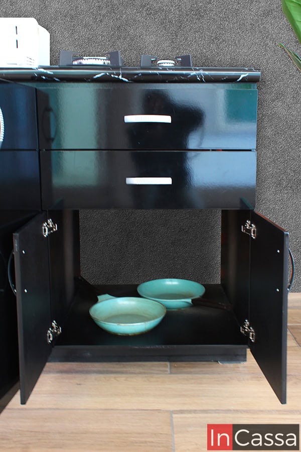 La imagen muestra el compartimento disponible en la sección de parrilla del módulo inferior. Este cuenta con un amplio espacio que conserva el mismo color negro que puede verse en el resto del módulo. La toma también permite observar de manera más cercana los cajones del mueble, así como algunos detalles adicionales tales como las jaladera de arco integradas en los cajones y puertas, así como las bisagras para la apertura y cierre de las ultimas.