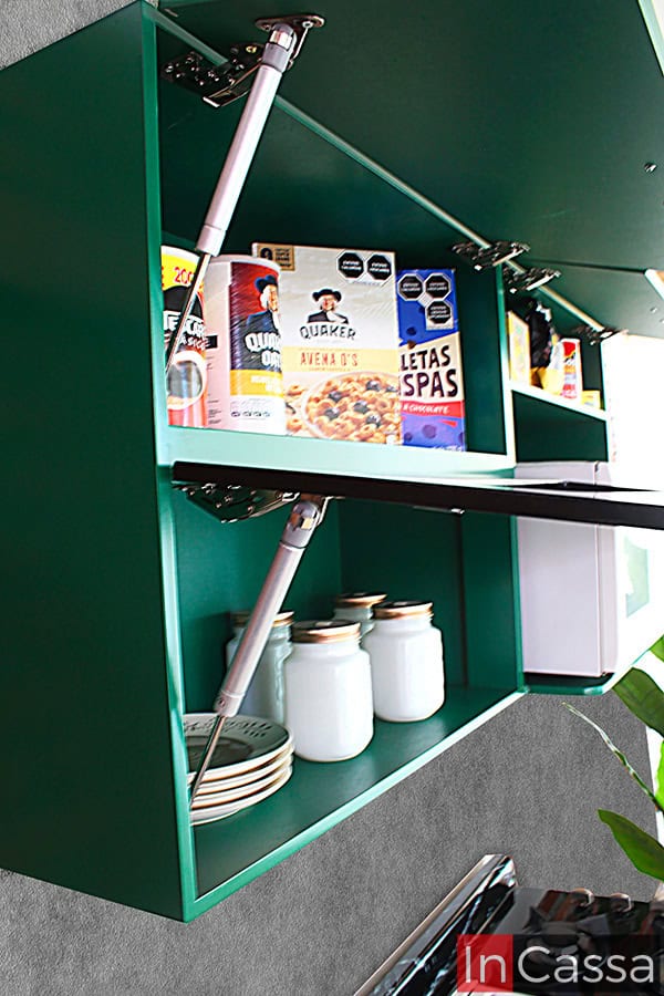 Toma lateral del módulo superior verde completo incluido en la cocina, en el que destacan sus compartimentos con puertas de apertura y cierre vertical gracias a pistones neumáticos, además de su espacio para microondas.