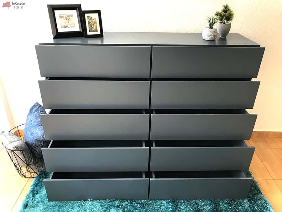 La imagen muestra todos los cajones de la cajonera Tel Aviv en color gris oxford completamente abiertos, destacando su gran capacidad de almacenamiento. Se aprecia en un entorno decorado con luz natural, sobre alfombra verde y con detalles ornamentales.