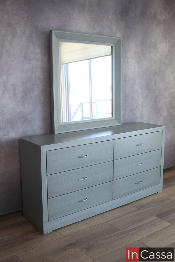 Una toma del tocador que nos permite ver su construcción lateral dejando a la vista el fondo del mueble así como el grosor del marco del espejo. La foto destaca el acabado cenizo claro aplicado uniformemente en cada parte del tocador.