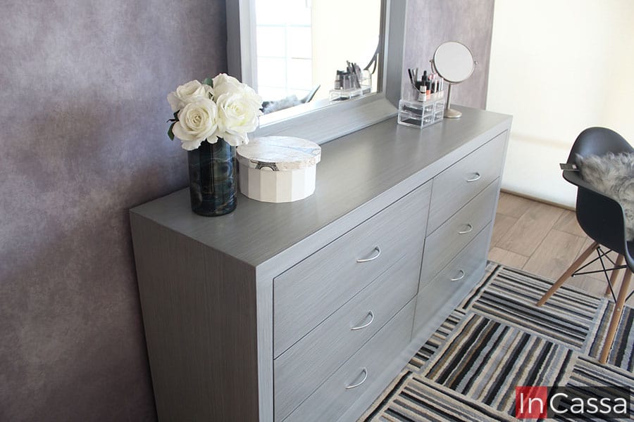 Una foto del tocador desde una toma lateral en la que se muestra de manera más detallada la construcción total del mueble, y en la que además se puede apreciar mucho mejor su acabado gris cenizo claro, así como detalles adicionales como son las jaladeras con forma de arco incorporadas a cada cajón.