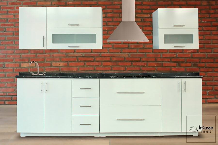 La imagen presenta una cocina integral en acabado blanco con cubierta de formaica tipo mármol negro, amplios módulos de almacenamiento y campana de acero inoxidable.