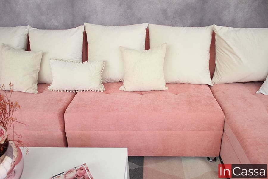 La toma muestra la sala suede rosa de frente, resaltando principalmente el love seat derecho junto con parte del love seat izquierdo y el chaise long izquierdo. también podemos observar los cojines grandes de suede hueso y algunos cojines decorativos pequeños del mismo tono. Cojines decorativos no incluidos en la sala.