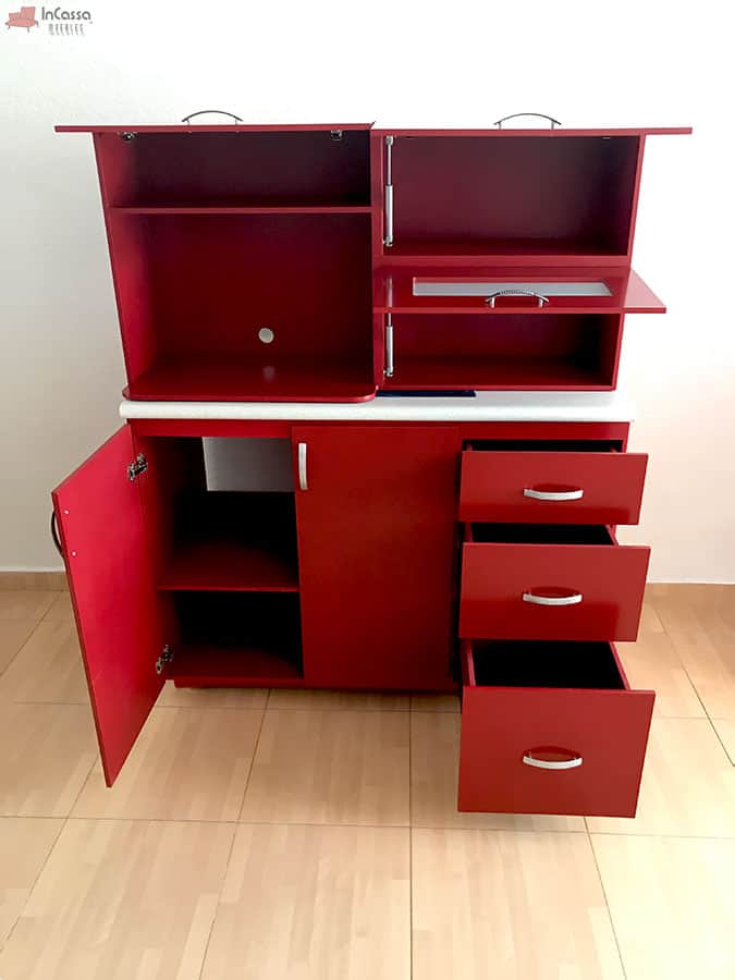 Una toma frontal del módulo inferior de la cocina con puertas y cajones abiertos revela su funcionalidad: tres cajones espaciosos y compartimento bajo tarja con división; mientras que la alacena superior presenta un área para microondas. El acabado rojo quemado y cubierta de formaica blanco fresh destacan visualmente.