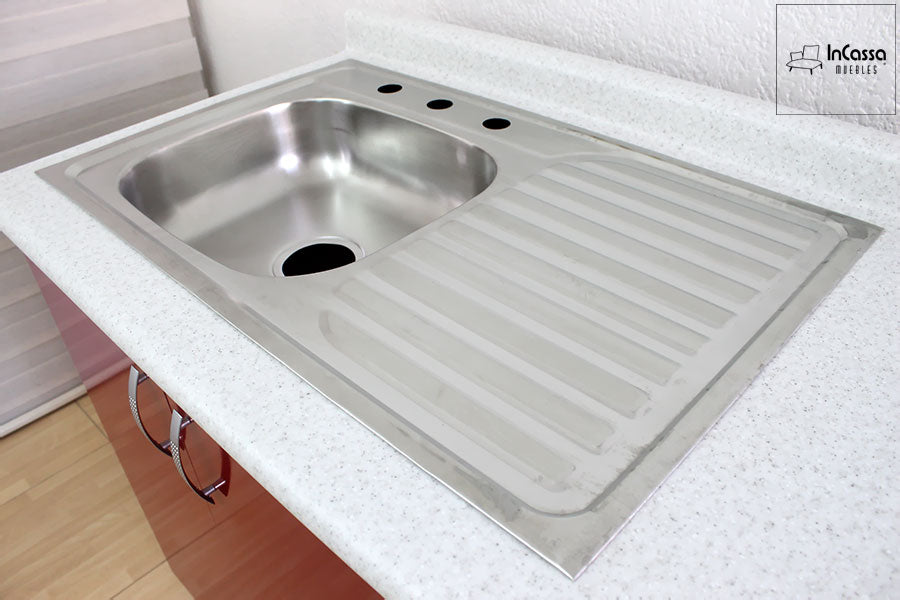 Una foto de la tarja incorporada al gran módulo inferior de la cocina, la cuál cuenta con una tina izquierda y un escurridor del lado derecho, toda fabricada en acero inoxidable. La toma también da una vista cercana de la cubierta de formica, en la que se puede apreciar mejor su acabado sal y pimienta.