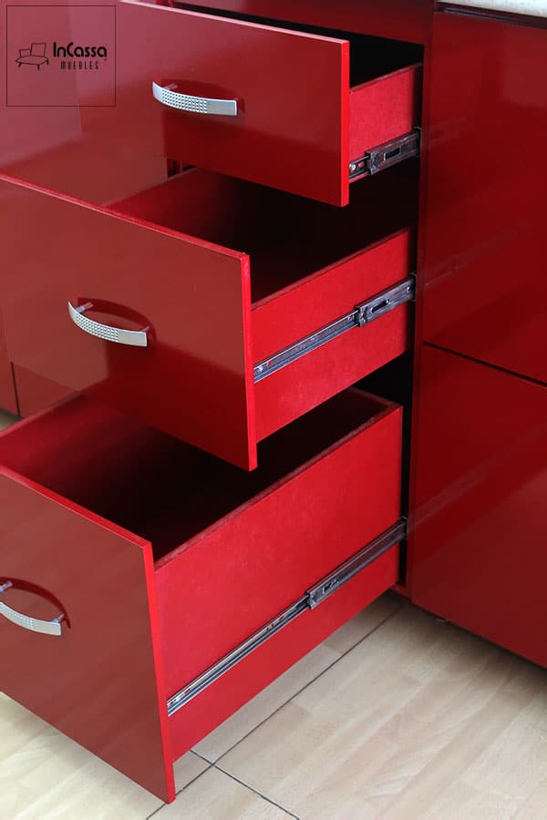 Vemos una toma que se enfoca en algunos de los cajones del módulo inferior, mismos que se presentan abiertos dejando ver su estructura completa pintada en color borgoña así como sus rieles metálicos incorporados, los cuales hacen posible la apertura y cierre de cada cajón. También se pueden apreciar de manera más detallada las jaladeras con forma de arco integradas a cada cajón, las cuales además resaltan el acabado brillante de la pintura.