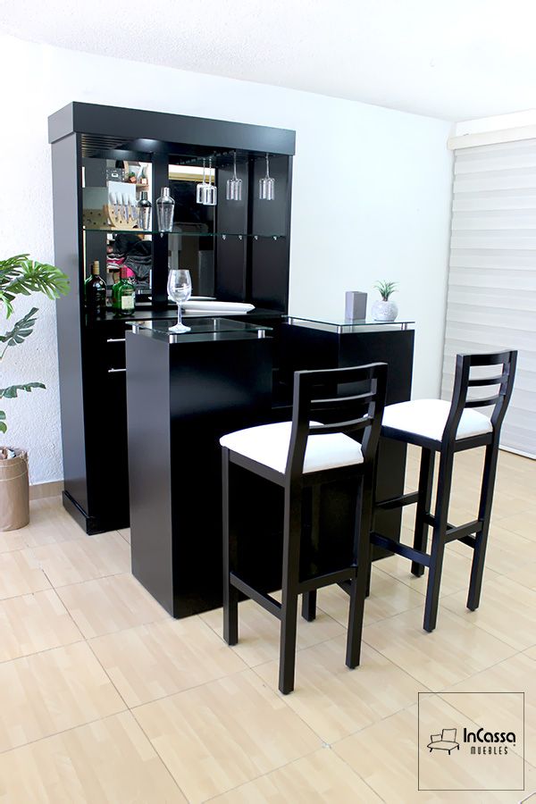 La imagen muestra una elegante cantina en acabado chocolate mate, vista en ángulo frontal. El mueble cuenta con una barra principal, repisas de vidrio, soporte para copas colgantes y espejo trasero que aporta profundidad. Se acompaña de dos bancos altos con estructura de madera en negro y asientos tapizados en blanco, ideales para complementar el diseño.