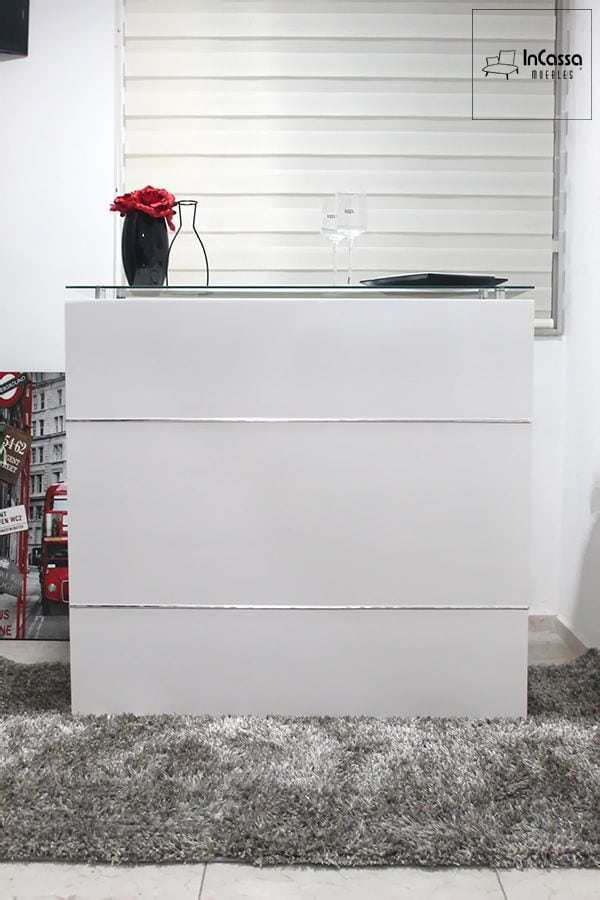 La fotografía presenta la Cantina Modelo UGANDA en elegante color blanco, con diseño minimalista y líneas horizontales cromadas. Su cubierta de cristal templado aporta amplitud visual y modernidad, ideal para crear un ambiente sofisticado y luminoso en cualquier área social.