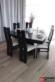 Fotografía lateral del elegante comedor triangular VIÑA DEL MAR en color chocolate con diseño contemporáneo. Incluye seis sillas de respaldo alto con líneas curvas y asientos tapizados en suede hueso, dispuesto con vajilla y centro de mesa decorativo, creando un ambiente sofisticado y acogedor.