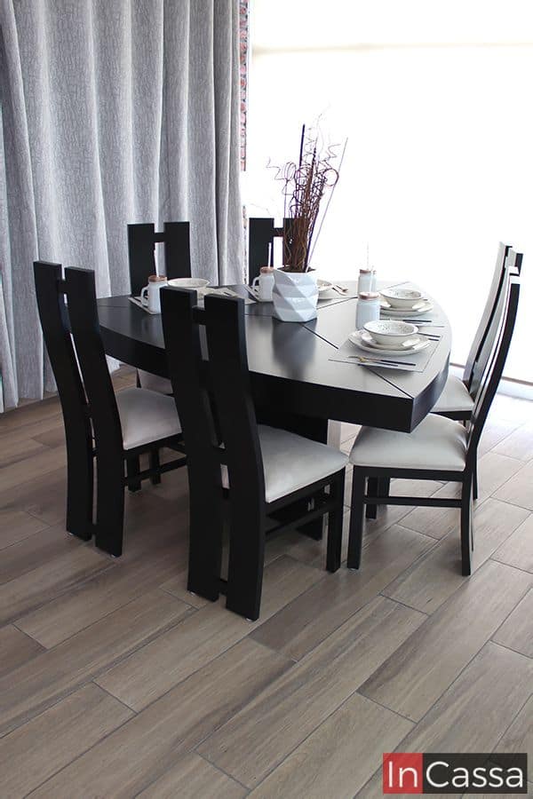 Fotografía lateral del elegante comedor triangular VIÑA DEL MAR en color chocolate con diseño contemporáneo. Incluye seis sillas de respaldo alto con líneas curvas y asientos tapizados en suede hueso, dispuesto con vajilla y centro de mesa decorativo, creando un ambiente sofisticado y acogedor.