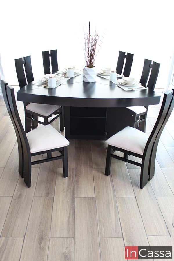 Imagen frontal del comedor chocolate con seis sillas tapizadas en suede hueso, destacando su mesa triangular con gabinete integrado en la base. La disposición formal incluye vajilla y centro de mesa decorativo, logrando un equilibrio entre elegancia y funcionalidad.