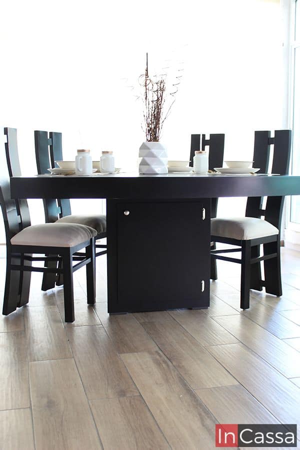 Fotografía frontal del comedor chocolate con seis sillas tapizadas en suede hueso, mostrando la mesa triangular con gabinete central cerrado. La decoración con vajilla y centro de mesa añade un toque sofisticado y funcional al conjunto.