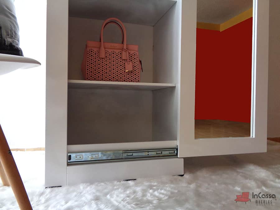 Esta toma resalta el detalle del estante inferior del armario zapatero blanco, ideal para guardar bolsos o artículos de mayor tamaño. El diseño incorpora rieles metálicos de alta calidad que aseguran un funcionamiento suave y duradero, complementando la funcionalidad y estilo del mueble.