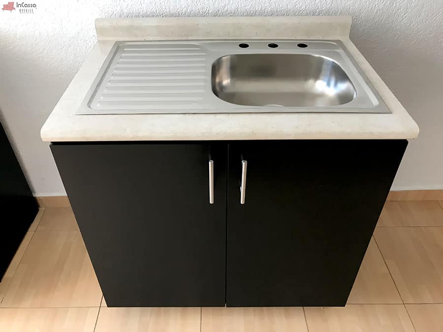 Este módulo de cocina incluye una tarja de acero inoxidable integrado en una cubierta de formaica estilo sal y pimienta, que combina funcionalidad y estilo. El gabinete inferior de puertas dobles ofrece un amplio espacio para almacenar productos de limpieza y utensilios. Las jaladeras metálicas y el acabado chocolate mate proporcionan un diseño moderno y elegante, ideal para cualquier cocina contemporánea.