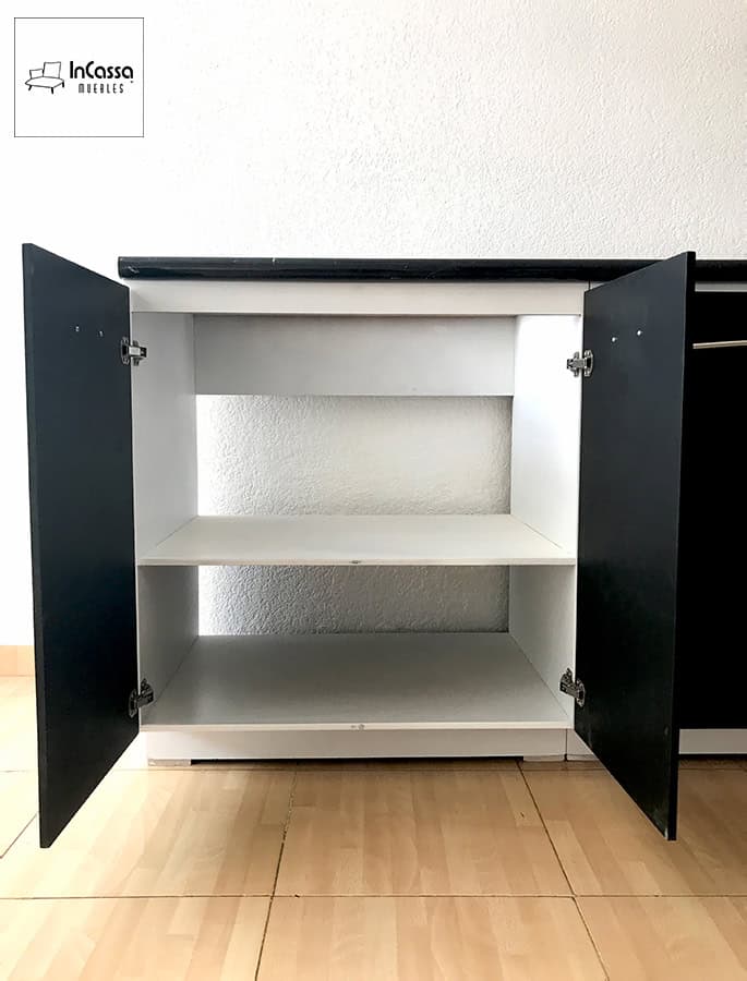 En esta imagen se aprecia el módulo izquierdo de la cocina integral BUGA para parrilla en una vista frontal completamente abierta, mostrando su estructura blanca con repisa central amplia para almacenamiento. Los frentes en tono chocolate permanecen abiertos, destacando el contraste con la cubierta de formaica estilo mármol negro y revelando un espacio perfecto para organizar vajilla, utensilios o recipientes de cocina.