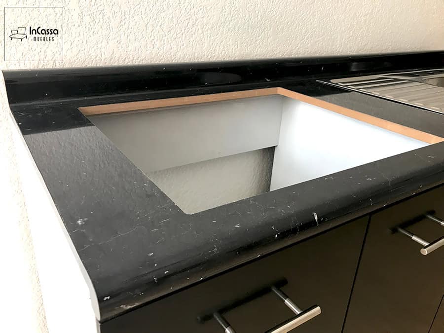 La imagen muestra una vista lateral del área donde se instalará la tarja, resaltando la cubierta de formaica estilo mármol negro con su borde redondeado y acabado brillante. Se aprecia el recorte perfectamente definido sobre estructura blanca, junto al escurridero metálico, destacando la calidad del diseño y la preparación para montaje.