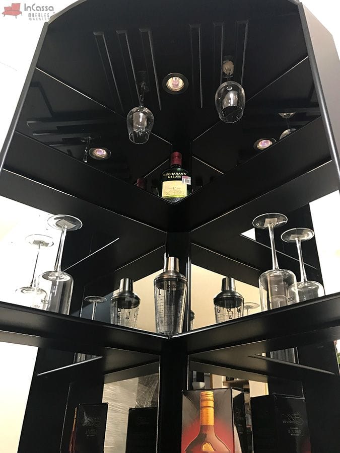 Con un enfoque moderno y minimalista, esta pieza de bar destaca por su estructura en chocolate mate y su integración de iluminación LED, resaltando cada detalle. El diseño incluye soportes para copas y espacios ideales para exhibir botellas y accesorios de bar, mientras que el espejo trasero añade profundidad visual al conjunto.