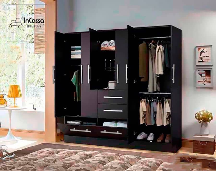 Moderno clóset de color chocolate completo, el cuál cuenta con muchos espacios diferentes para almacenar todo tipo de ropa. El mueble se encuentra instalado en una amplia estancia de estilo minimalista, de paredes blancas con detalles decorativos y piso de madera.