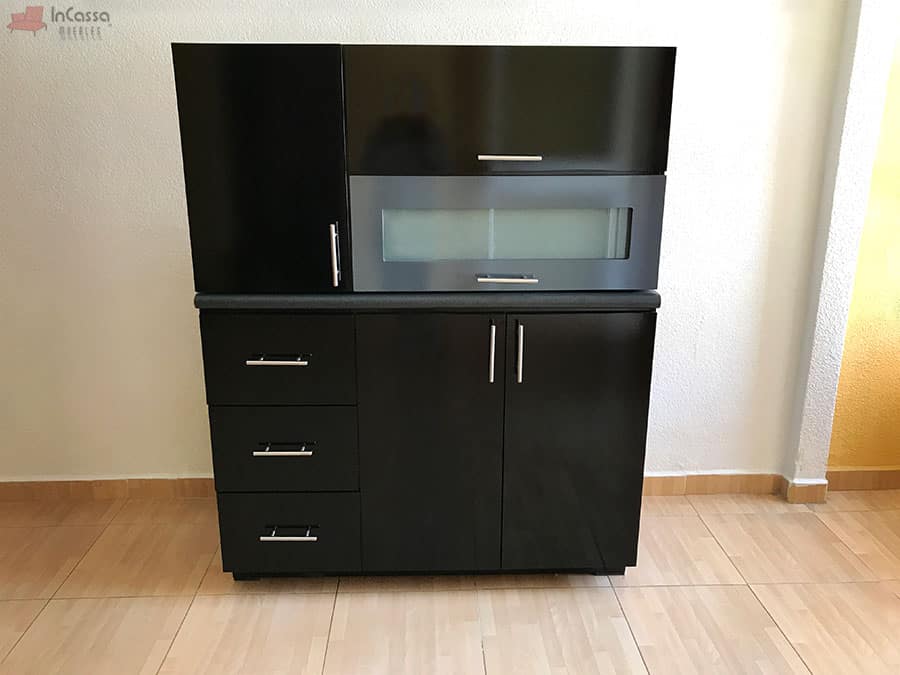 Se presenta la alacena superior de la Cocina Integral Irlanda para Estufa en elegante color negro brillante, colocada sobre el módulo inferior de tarja. Destaca la puerta abatible con cristal esmerilado, combinada con repisas internas que aportan funcionalidad y estilo. La cubierta de formaica en mármol negro completa un conjunto moderno y sofisticado.