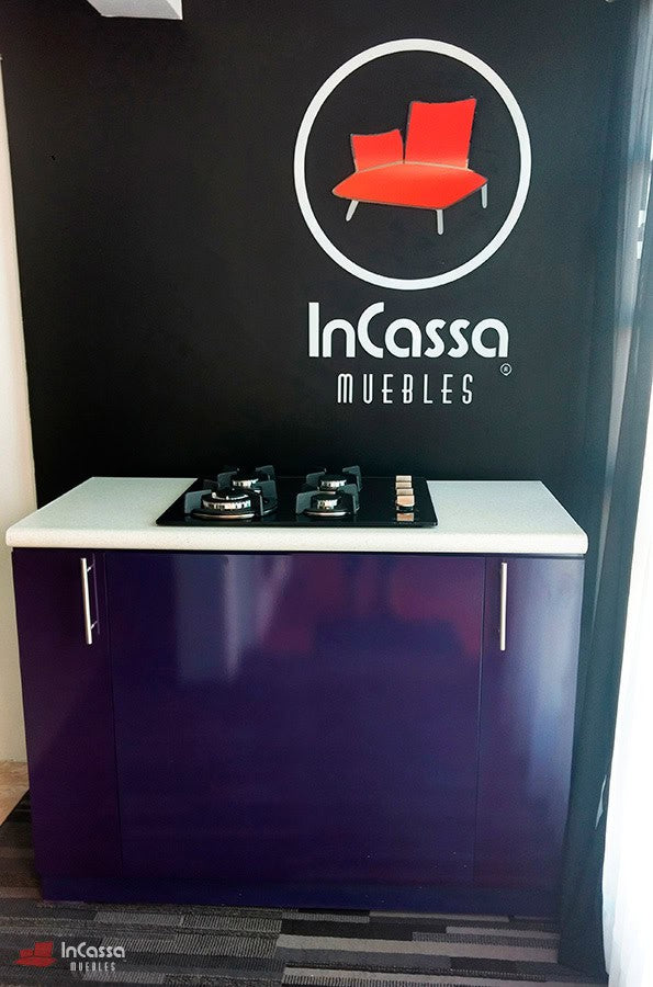 Se presenta una toma frontal de la Isla LOMBARDIA, en tono morado brillante. Con cubierta de formaica blanca con parrilla empotrada de 4 quemadores, jaladeras metálicas y base con zoclo integrado.