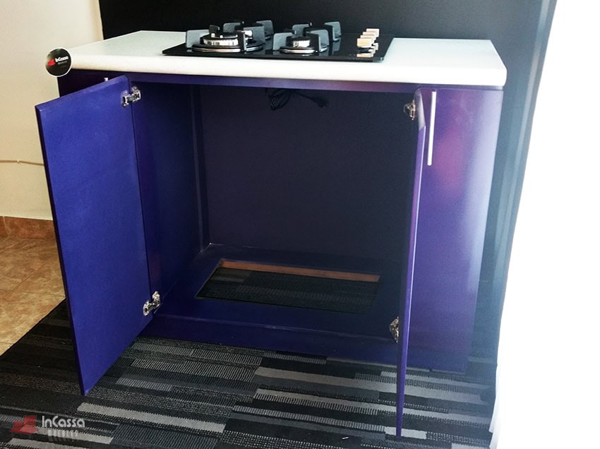 En esta imagen se observa la Isla para Parrilla Modelo LOMBARDIA desde un ángulo lateral, con ambas puertas abiertas. La fotografía revela el amplio espacio interior destinado para la instalación de conexiones de gas o eléctricas, facilitando su funcionalidad. Destaca el vibrante acabado en color morado brillante y la cubierta blanca de formaica.