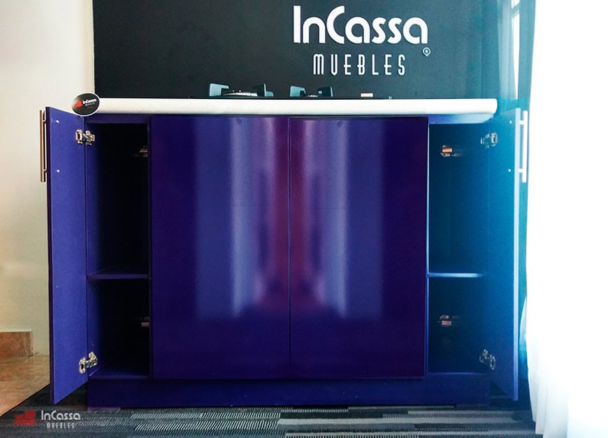 La fotografía muestra la Isla para Parrilla Modelo LOMBARDIA con sus puertas completamente abiertas, permitiendo apreciar los compartimentos internos divididos en secciones con repisas, ideales para almacenar utensilios o artículos de cocina. El acabado en tono morado brillante y herrajes metálicos resalta su diseño moderno.