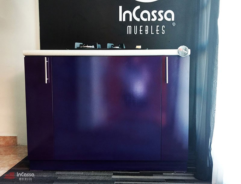 La imagen muestra una toma centrada de la Isla LOMBARDIA, destacando el acabado morado brillante del módulo inferior con puertas cerradas, cubierta blanca de formaica y jaladeras metálicas verticales.