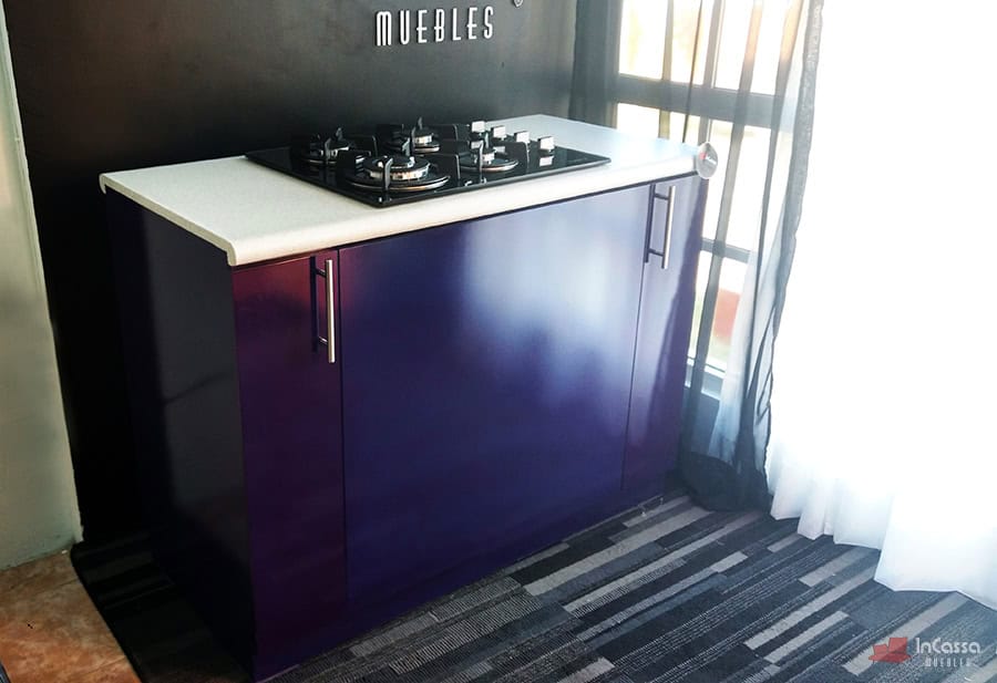 En esta imagen se aprecia la Isla LOMBARDIA desde una perspectiva lateral en ángulo, destacando el elegante color morado del mueble, la cubierta de formaica blanca y la parrilla empotrada de cuatro quemadores.