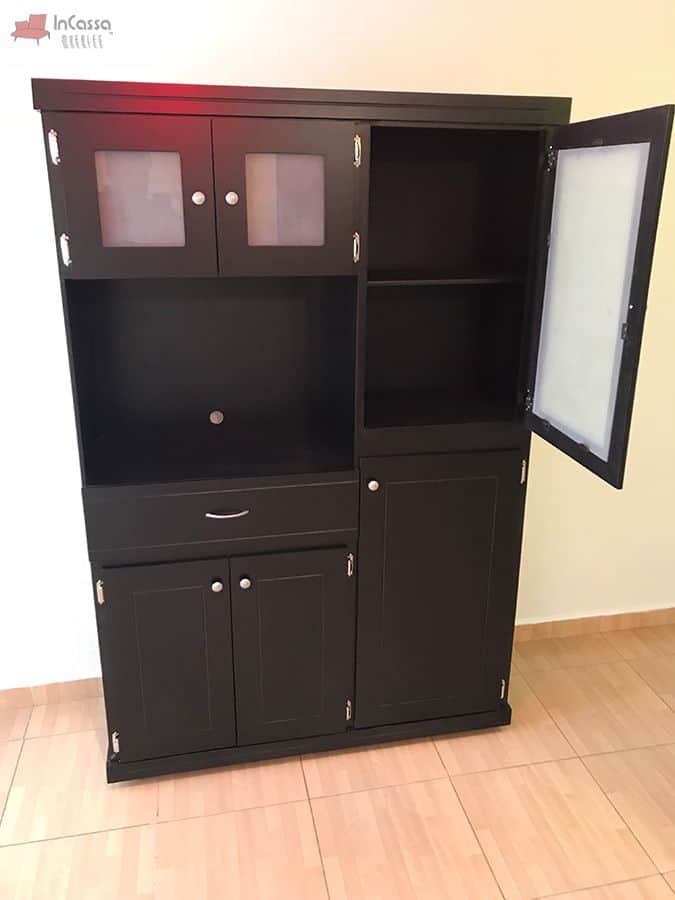 La imagen presenta la puerta lateral de cristal esmerilado completamente abierta, exhibiendo dos amplias repisas internas, ideales para almacenar vajilla o despensa. El acabado chocolate brinda un contraste sofisticado con el piso claro.