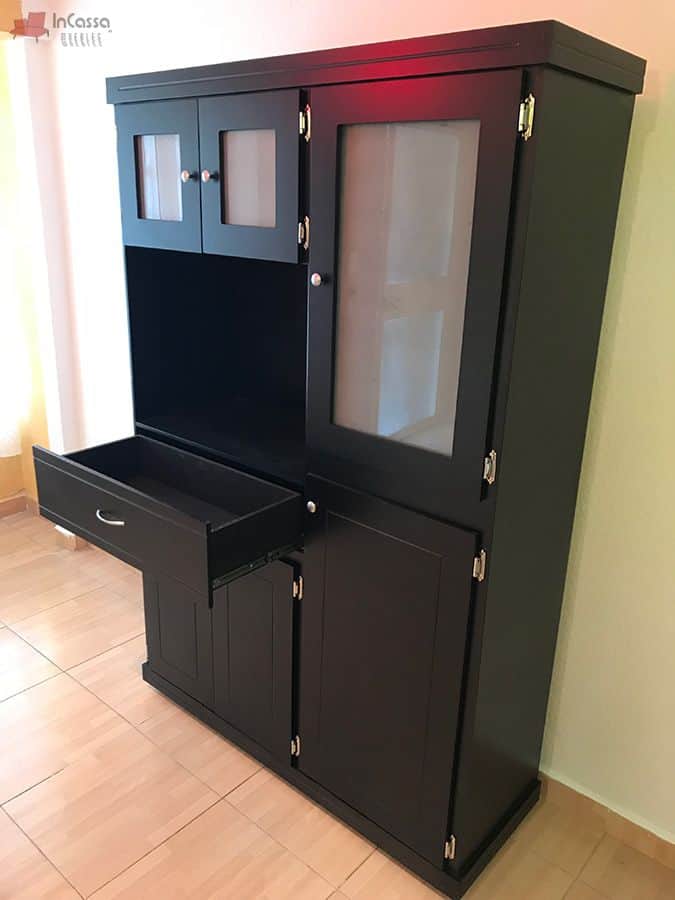 Una toma muestra el cajón central completamente abierto, ideal para utensilios o cubiertos. La estructura robusta y los detalles metálicos destacan sobre el acabado chocolate elegante del diseño.