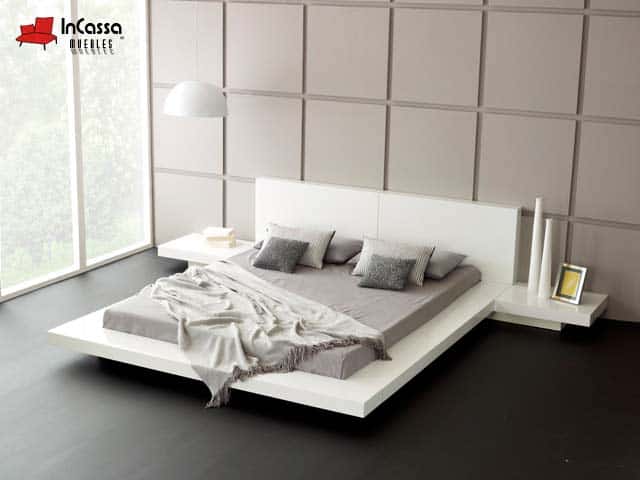La imagen presenta una cama moderna estilo minimalista en blanco con cabecera recta y burós flotantes. Su diseño de plataforma baja con líneas limpias y tonos neutros aporta amplitud, elegancia y equilibrio visual al espacio.