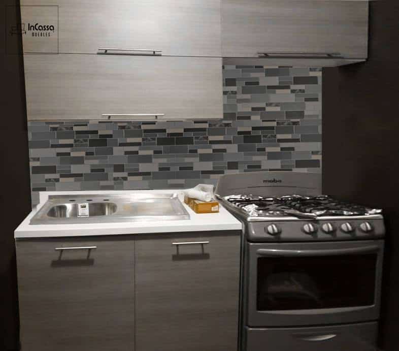 La imagen muestra la Cocina Integral Modelo PISA, diseñada para estufa en tonos gris cenizo oscuro. Incluye módulo inferior con tarja de acero inoxidable, cubierta de formaica blanco fresh y espacio para estufa de 30”. El contraste con el azulejo tipo mosaico en grises le da un toque moderno y elegante.