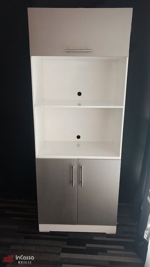 La imagen muestra el mueble para horno Windsor en acabado blanco y silver visto de frente, con puertas superiores e inferiores cerradas y estantes centrales vacíos. Presenta perforaciones circulares en la parte posterior para el paso de cables y jaladeras metálicas rectas que aportan un toque moderno.