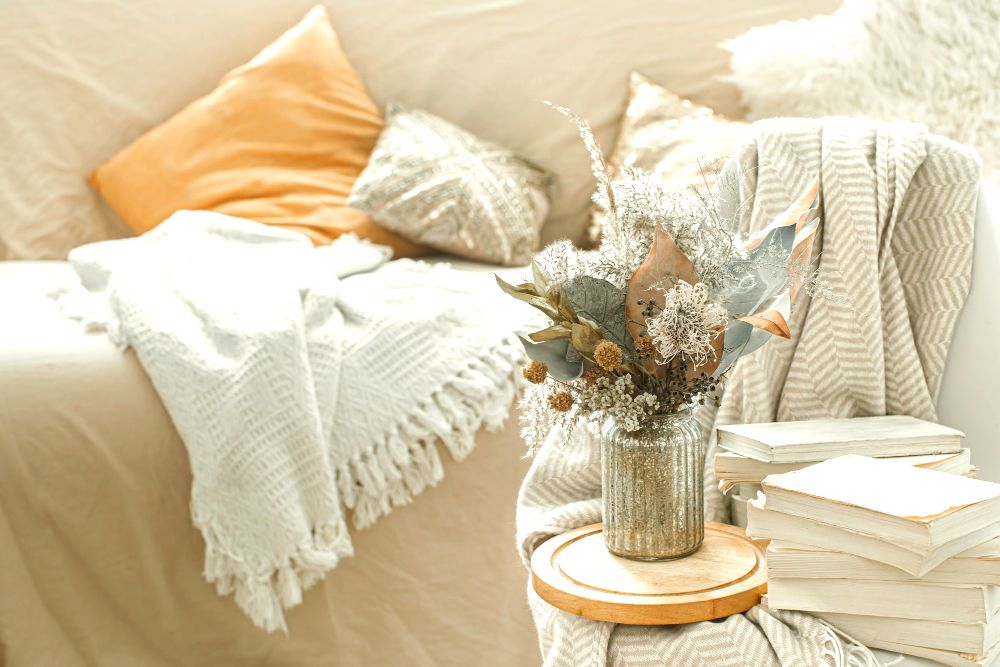 La foto nos muestra un love seat decorada con un cubre sala y cobijas de color crema con cojines decorativos en tono mantequilla.