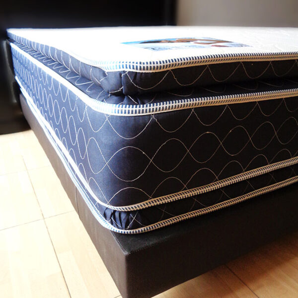 Colchón de doble colchoneta apoyado en una base con tapiz chocolate, el acolchonado del colchón es hueso y los bordes de tono azulado.