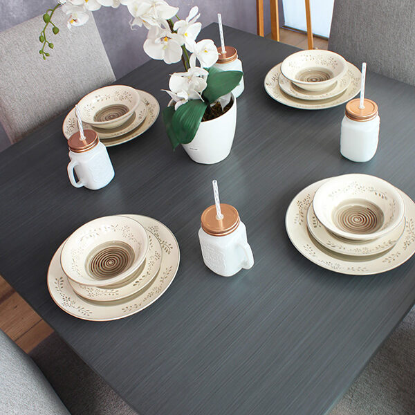 Se presenta la mesa en acabado gris cenizo oscuro de comedor decorada con vajilla y un centro de mesa con orquídeas blancas, creando un ambiente elegante y acogedor, ideal para cenas formales y casuales.